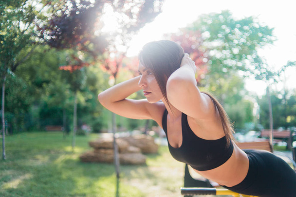 Mujer sana con ropa deportiva haciendo ejercicio en máquinas de ejercicios al aire libre. - Foto, imagen