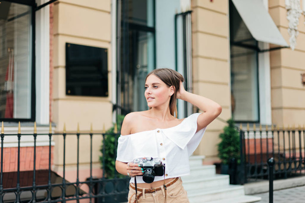 Cheerful blond woman holding retro camera in the urban environment - Foto, Imagem