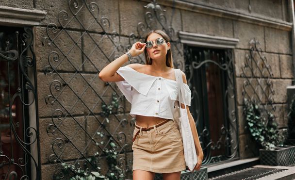 Katumuoti. Muodikas tyylikäs nainen trendikkäissä vaatteissa ja aurinkolaseissa, jotka aiheuttavat ulkona vanhan arkkitehtuurin taustaa vasten
 - Valokuva, kuva