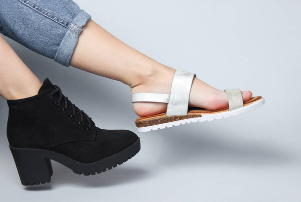 Ženské nohy v džínách spoutané v botách a sandálech sedí na bílém pozadí. Kreativní módní snímek - Fotografie, Obrázek