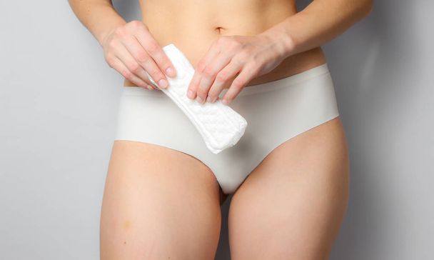 Beauty studio shot. Slim woman in white panties holds sanitary pad on gray background. Feminine hygiene concept - Photo, Image