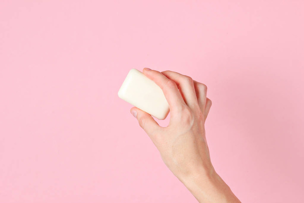 Γυναικείο χέρι κρατώντας κομμάτι σαπούνι σε ροζ φόντο. Άνω όψη - Φωτογραφία, εικόνα