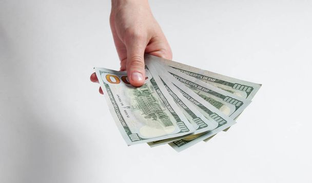Mão feminina segurando notas de cem dólares em um fundo branco. Conceito financeiro minimalista do orçamento familiar
 - Foto, Imagem