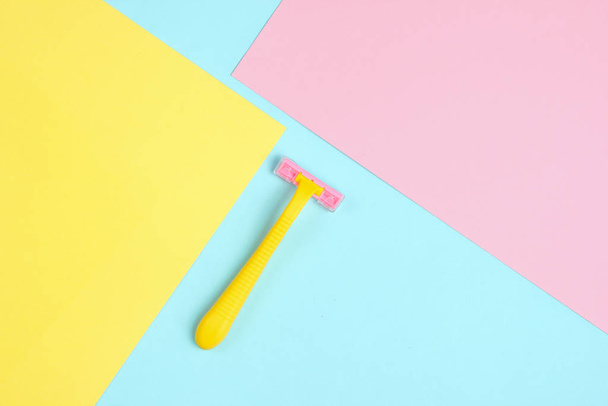 minimalistisches Schönheitskonzept. Epilation. Gelber Rasiermesser aus Kunststoff auf pastellfarbenem Hintergrund. Ansicht von oben - Foto, Bild