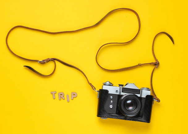 Koncepcja minimalizmu turystyki. Vintage retro aparat fotograficzny w skórzanej pokrywie z paskiem na żółtym tle z podróży słownej. Widok z góry - Zdjęcie, obraz