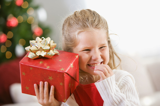 Kerstmis: Jong meisje houdt kerstcadeau aan oor - Foto, afbeelding