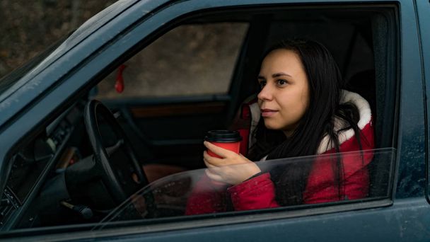 Woman drinks coffee in the car. Young woman drinking coffee while driving her car - Fotografie, Obrázek