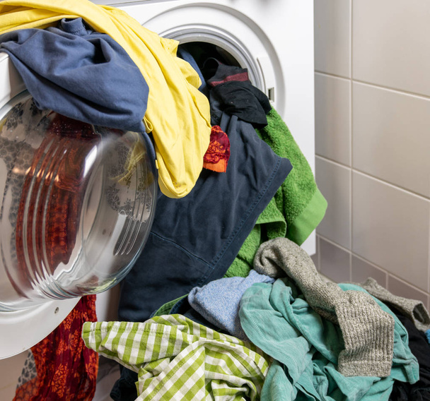 гигантская куча разноцветного грязного белья и стиральная машина, набитая одеждой
 - Фото, изображение