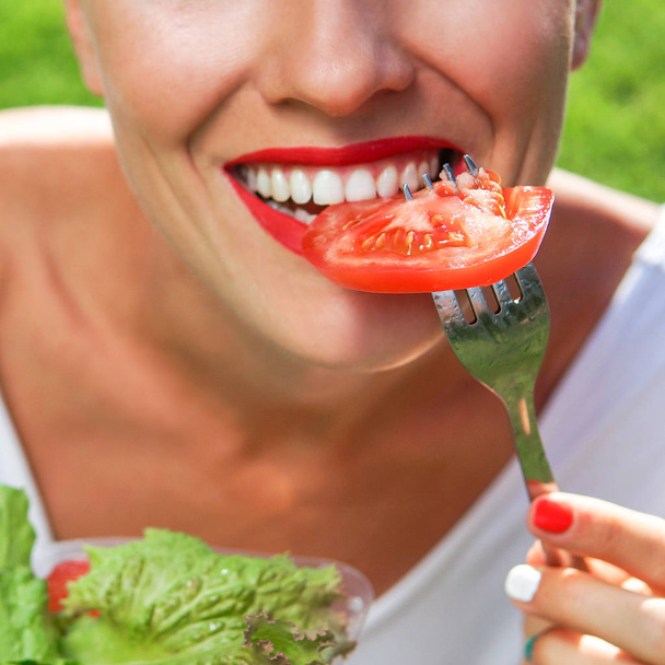 Beautiful caucasian woman eating salad over green natural background - 写真・画像