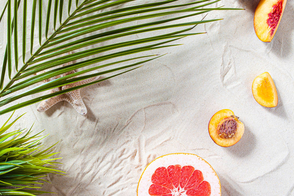 Пляжный отдых. Пальмовый лист, морская звезда, ветвь белого дерева и сочные фрукты лежат на белом мелком песке. Обои для рабочего стола. - Фото, изображение