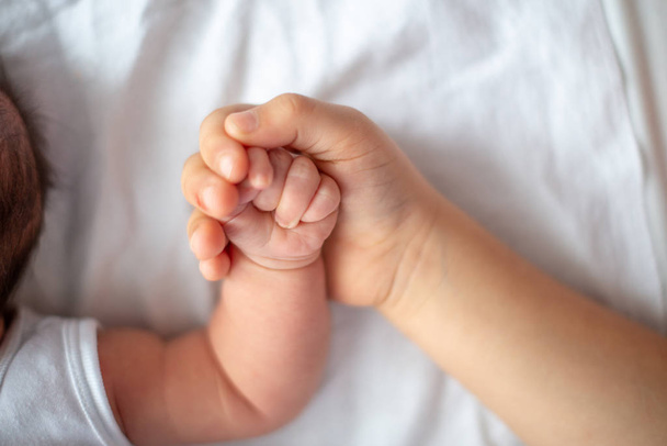 Közelkép egy testvérkézről, aki egy hónapos kishúga kezét fogja. Felülnézet - Fotó, kép
