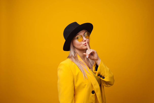Shhh, gesturefinger near lips, mystery and secret. Stylish trending young woman in bright clothes on yellow background, - Fotó, kép