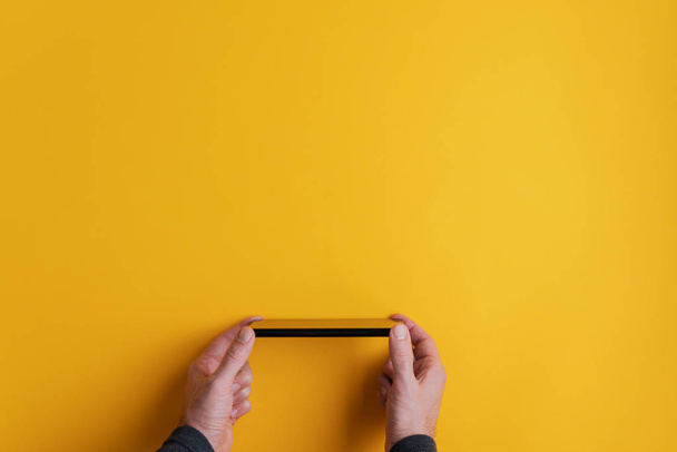 Mano masculina sosteniendo teléfono inteligente negro sobre fondo amarillo
 - Foto, Imagen