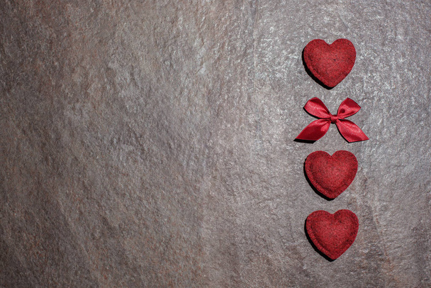 Sevgililer Günü için arka plan, 3 kırmızı vintage kalp ve bir fiyonk dokulu, pürüzlü, taş bir arka plan - Fotoğraf, Görsel