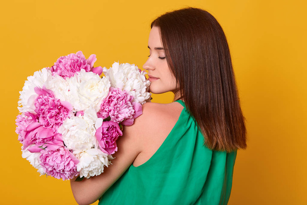 Woman with bouquet of pink and white peonies in hands, posing backwards, girl in light transparent dress. Dark haired lady holding her present for St. Valentines Day, female smelling flowers. - Foto, afbeelding