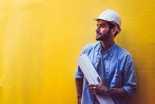 Young engineer carry blueprint at yellow background - 写真・画像
