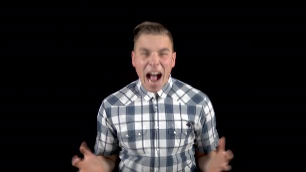 The young man is screaming. A man screams strongly in a shirt on a black background - Footage, Video