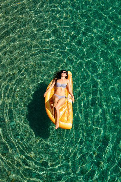Slim young woman in bikini and sunglasses on the air mattress floats in the open sea. - Foto, immagini