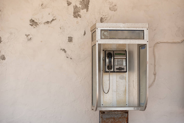 Vintage pay public use phone cabin on white ragged wall - Photo, Image