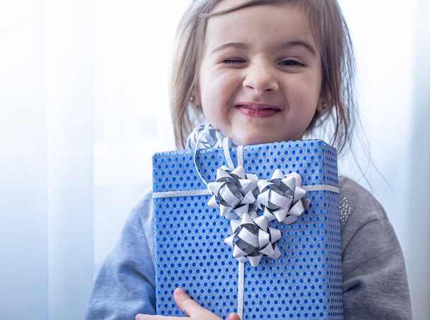 ein kleines Mädchen mit einem blauen Urlaubsgeschenk. - Foto, Bild
