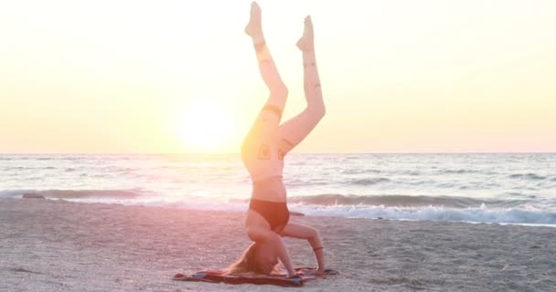 Mladá žena v teplákové soupravě cvičí jógu na pláži nad mořem při úžasném východu slunce. Fitness, sport, jóga a zdravý životní styl koncepce. Zpomalený pohyb. - Záběry, video