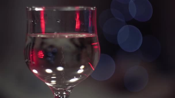 Kerstmis, Nieuwjaar, feestdagen. Bubbels in champagne glas tegen de achtergrond van flikkerende gekleurde lichten. Achtergrond video. Langzame beweging. Sluit maar af. Blauwe wijting. - Video