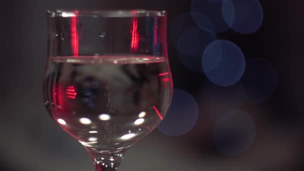 glas champagne met bubbels, verlicht door rood licht, staat schittering, bokeh van knipperende lichten, op de achtergrond. - Video