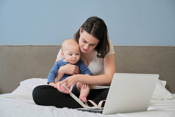 Mãe com fita de centímetros medindo seu bebê sentado em casa
 - Foto, Imagem