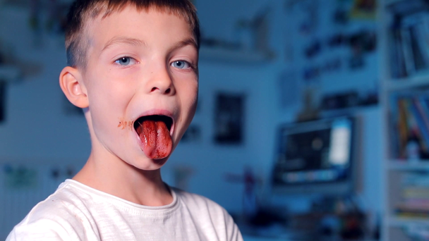 the boy eats chocolate, then shows the chocolate tongue - Filmati, video