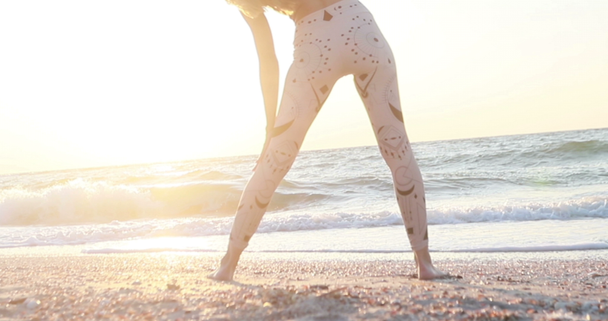 Jonge vrouw in bodysuit oefenen yoga op het strand boven zee bij verbazingwekkende zonsopgang. Fitness, sport, yoga en een gezonde levensstijl concept. Langzame beweging. - Video