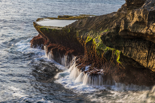 Outcrop at Devil's Tear, on the shore of Nusa Lembongan island, Bali, Indonesia. Tide pool on top of the rocky cliff; water streaming from the rocks back into the ocean.  - Foto, Imagen