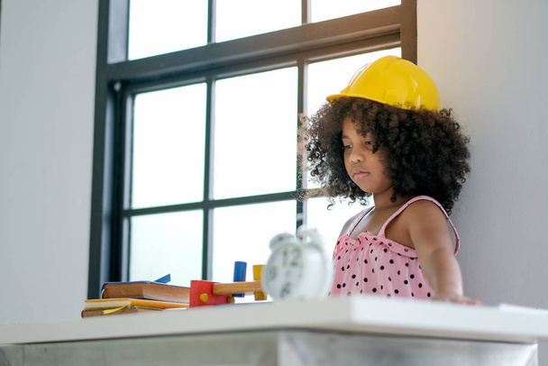Портрет молодої африканської дівчини грає в якості інженера, носячи жовтий капелюх у вітальні з деякими прикрасами.. - Фото, зображення