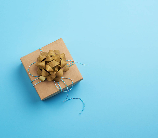καφέ τετράγωνο κουτί με ένα δώρο δεμένο κορδέλα με ένα τόξο σε ένα μπλε ba - Φωτογραφία, εικόνα