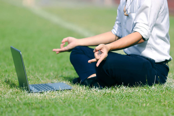 Entspannter junger asiatischer Geschäftsmann mit Laptop macht Yoga auf dem Feld. - Foto, Bild