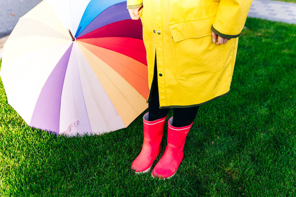 žlutý plášť. Gumově růžové boty proti. Koncepční obraz nohou v botách na zelené trávě. deštník - Fotografie, Obrázek