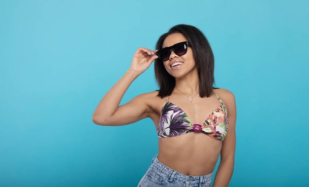 Cheerful african american woman in swimsuit and sunglasses on blue studio background. - Foto, imagen