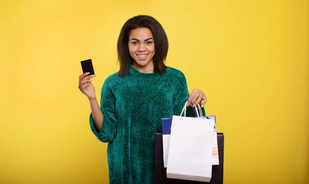 Beautiful African-American woman with shopping bags and credit card on color background. - Фото, зображення