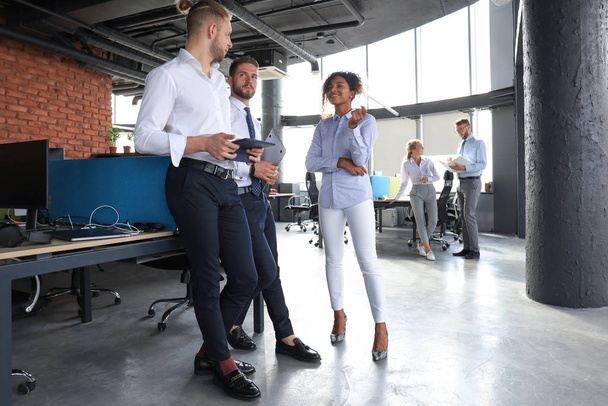 Skupina moderních obchodních lidí mluví a usmívají se, když stojí v kanceláři - Fotografie, Obrázek