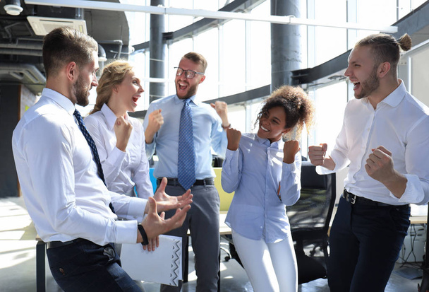 П'ять щасливих сучасних бізнесменів тримають зброю піднятою і виражають радість, стоячи у великому офісі
 - Фото, зображення