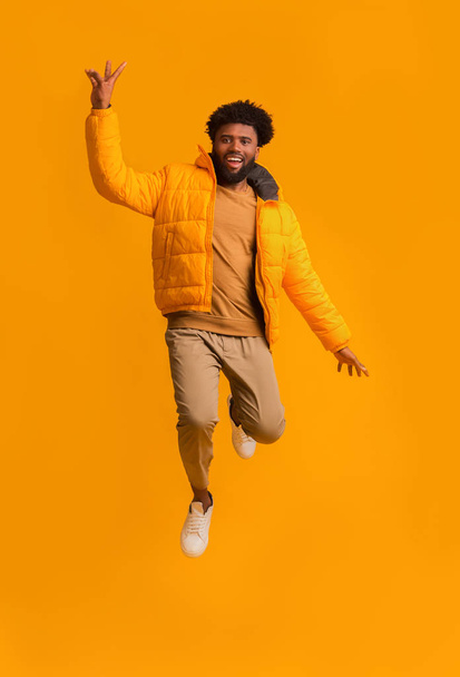 Emocionado hombre afro en brillante chaqueta de invierno saltando
 - Foto, Imagen
