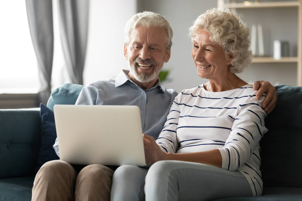 Aged spouses sitting on couch watching movie using laptop - Photo, Image