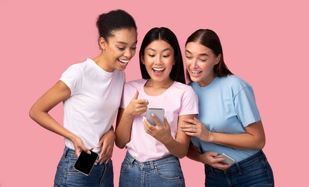 drei Mädchen mit Smartphone, die Freunden eine Anwendung empfehlen, rosa Hintergrund - Foto, Bild