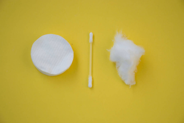 Καθαρίστε λευκό βαμβάκι για τον καθαρισμό στο μακιγιάζ, και το αυτί κολλάει σε κίτρινο φόντο - Φωτογραφία, εικόνα