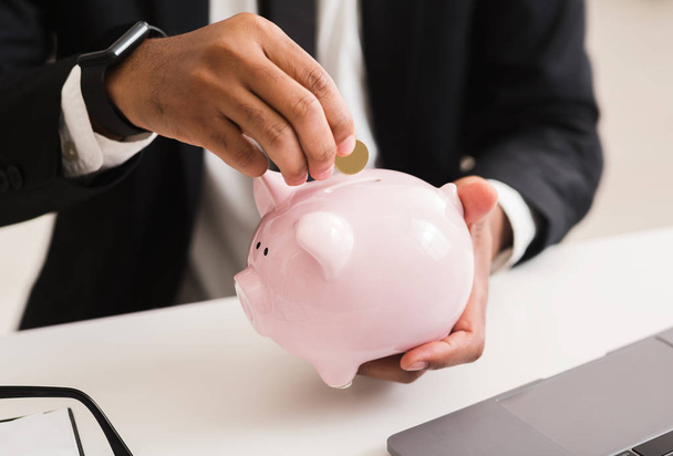 Man in suit putting coin into pink piggy bank - Φωτογραφία, εικόνα