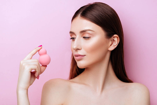 Funny girl holding pink sponge near her face. Portrait of young girl on pink background. - Foto, imagen