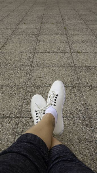 Vrouwen voeten dragen witte mode sneaker schoenen in hipster stijl. Negatieve ruimte. Kopieer ruimte voor tekst.  - Foto, afbeelding