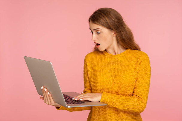 Portrait of astonished ginger girl in sweater holding laptop and - Φωτογραφία, εικόνα