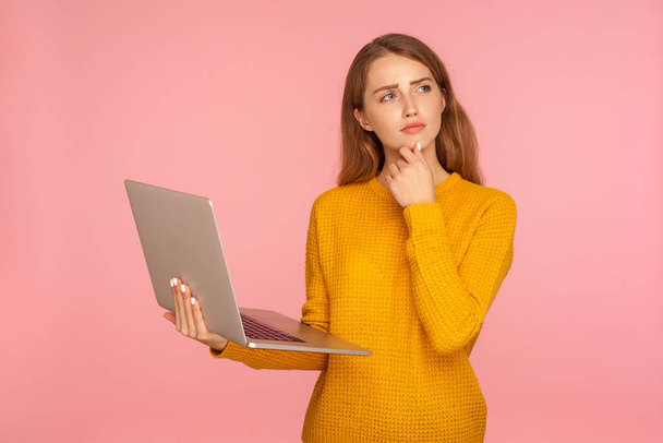 Portrait of thoughtful ginger girl in sweater holding laptop and - Foto, Bild