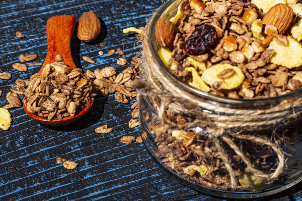 Granola with dried fruits in a glass jar and a wooden spoon on a blue wooden background. - Foto, immagini
