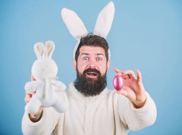 Feeling excited about Easter. Hipster with long rabbit ears holding egg laying hare. Easter bunny delivering colored eggs. Celebration of spring holiday. Bearded man with bunny toy and Easter egg - Foto, imagen